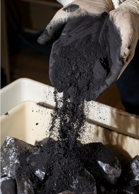 Hender som drysser svart silisiumstøv ned i en container.