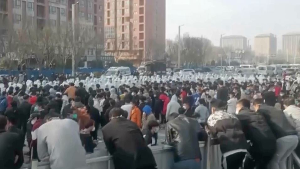 Dette bildet fra onsdag 23. november viser demonstranter som står ansikt til ansikt med sikkerhetspersonell i hvite beskyttelsesdrakter på fabrikkområdet til Foxconns største Iphone-fabrikk i Zhengzhou.