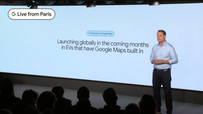 Chirs Phillips står forn en stor skjerm. På skjermen står det "EV Features in Google Maps, Launching Globally in the comming months in EVs that ahve Google Maps built in"
